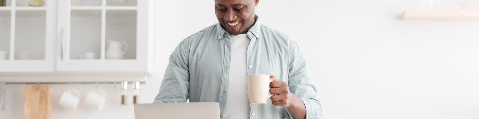 Man looking at laptop holding a mug in his hand.